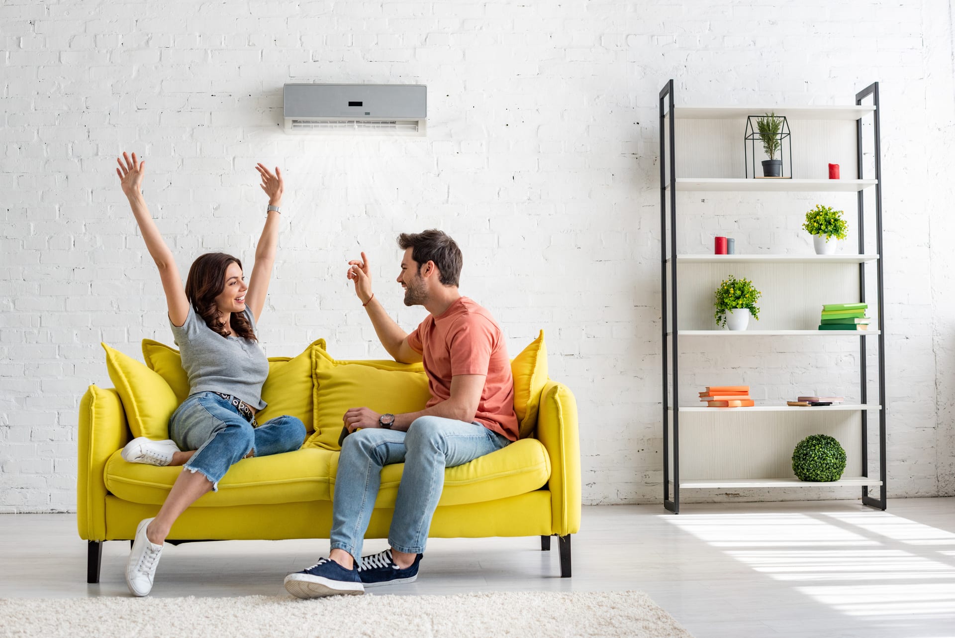 happy man and woman talking while sitting on yellow sofa under air conditioner at home